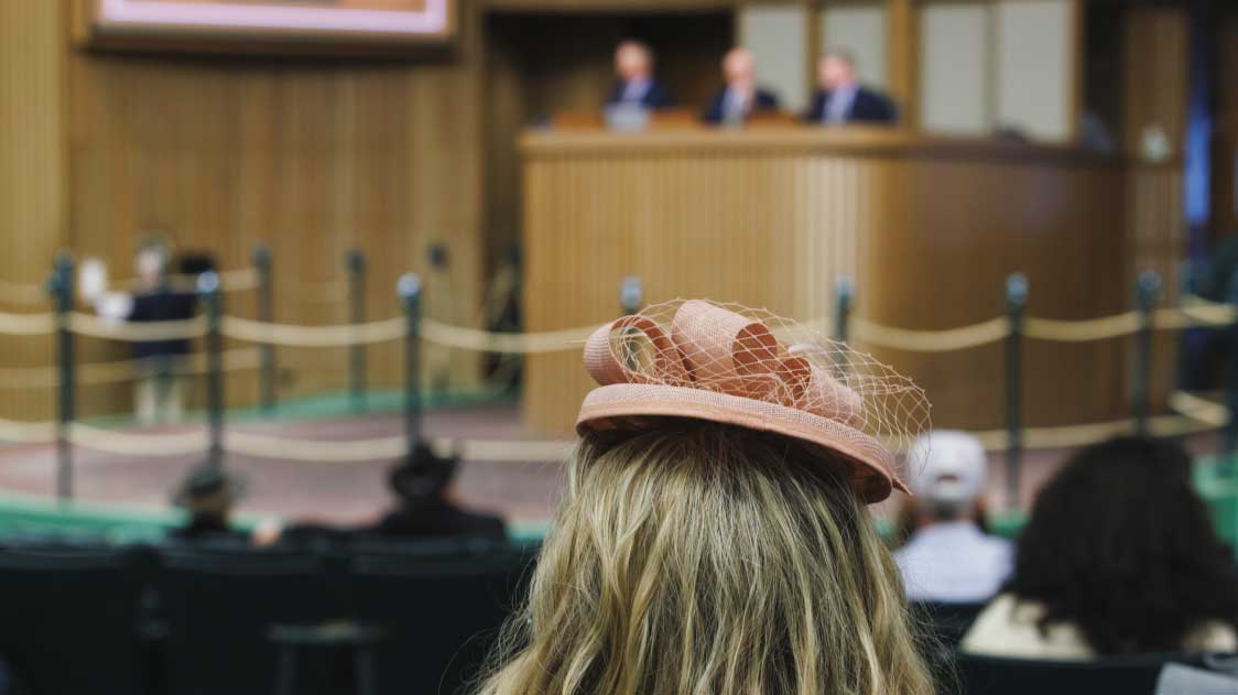 Woman wearing an elaborate hat seated in the sales arena at Keeneland